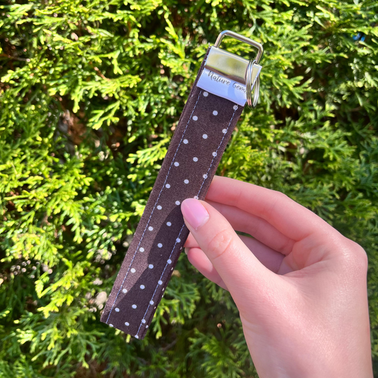 Hand holding a brown strap with white polka dots against a green bush background