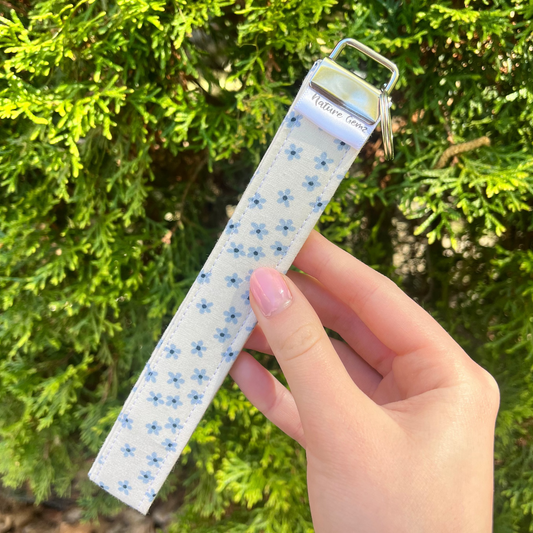 Hand holding a patterned keychain with a green bush in the background