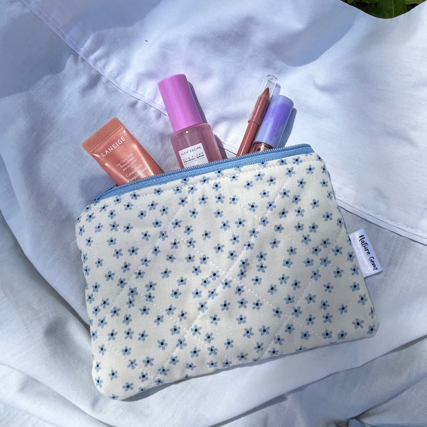Small pouch with cosmetic items on a white surface with grass in the background