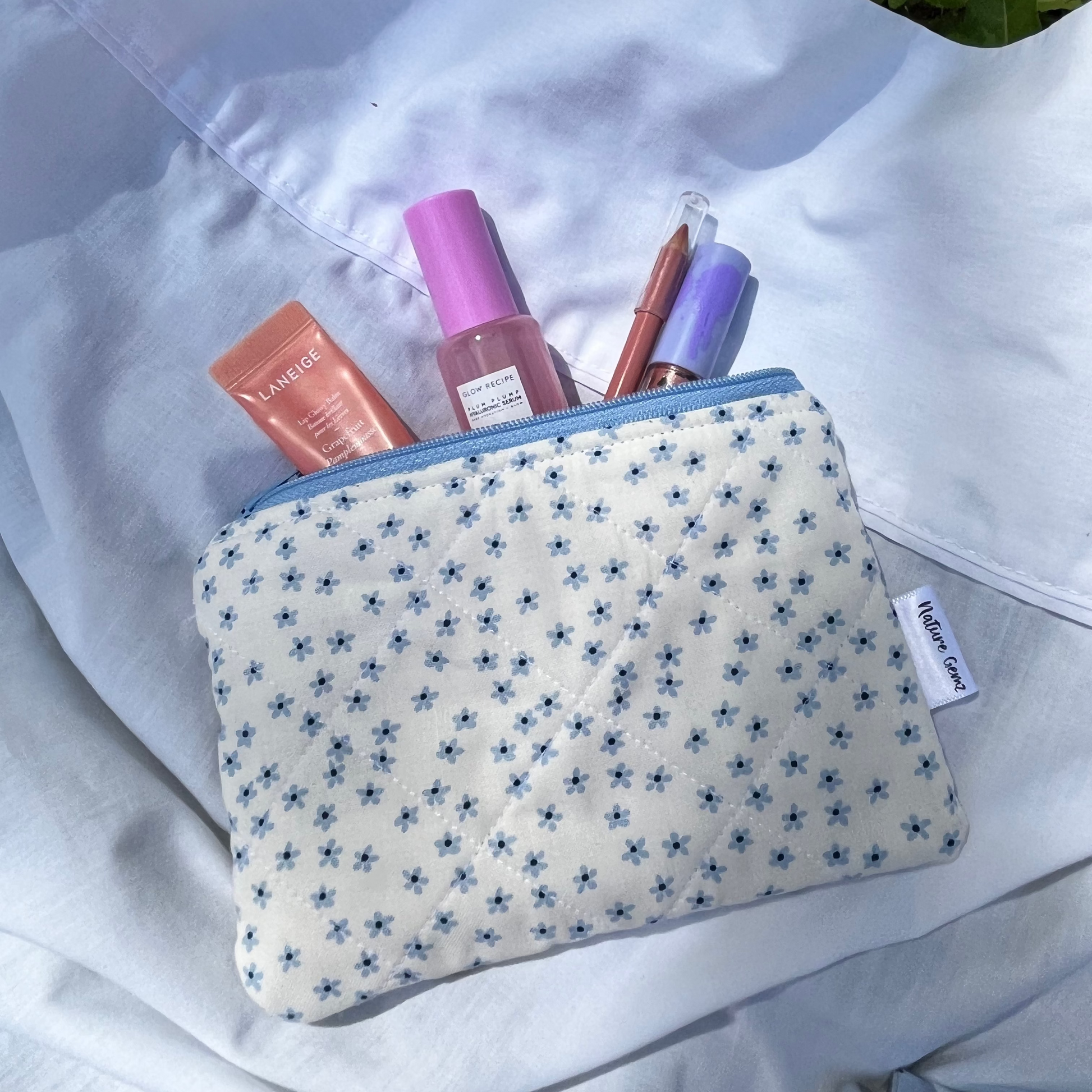Small pouch with cosmetic items on a white surface with grass in the background