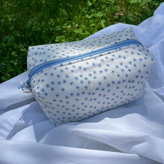 Small pouch with blue zipper on a white fabric background with greenery in the background
